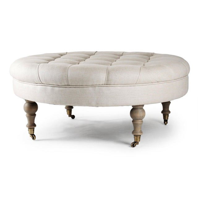 The Maison Tufted Round Ottoman from Zentique features a generous round button-tufted top on turned wood legs with brass...