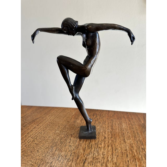 Elegant bronze figure of a nude female dancer balancing gracefully on one foot, arms extended in motion. This piece bears...
