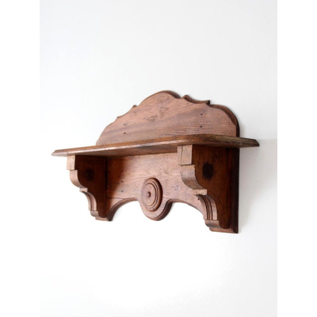 An early 20th-century folk art wall shelf featuring a shaped crest, carved rosette detailing, and architectural brackets....