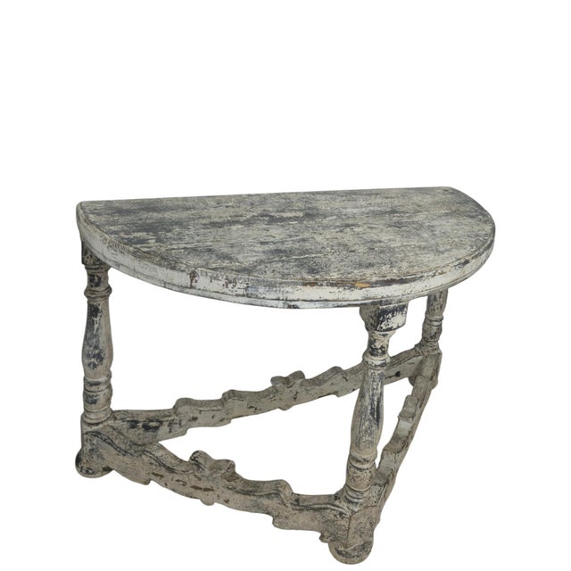 A refined pair of highly decorative demi-lune wall consoles finished in a soft gray-white painted surface. Each console...