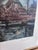 This original vintage landscape print, created around 1970, shows a peaceful river with trees, a boat and a cottage along...