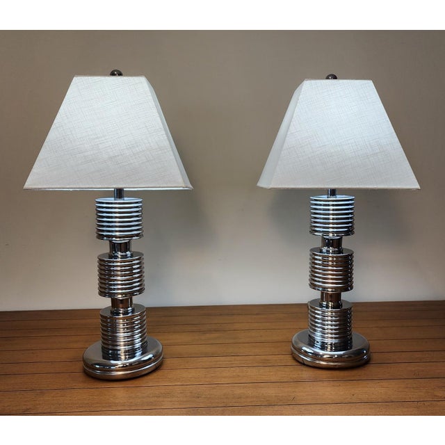 Striking Art Deco Revival pair of chrome table lamps in the Style of Karl Springer. The tiered, cylindrical body features...