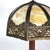 This antique table lamp, in the manner of Bradley & Hubbard, features an 8-panel slag glass shade with intricate overlay...