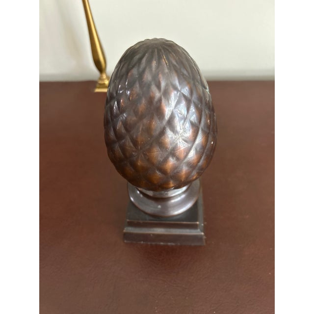 This cast metal pineapple finial garniture statue features a rich bronze-tone patina atop a stepped square pedestal base....