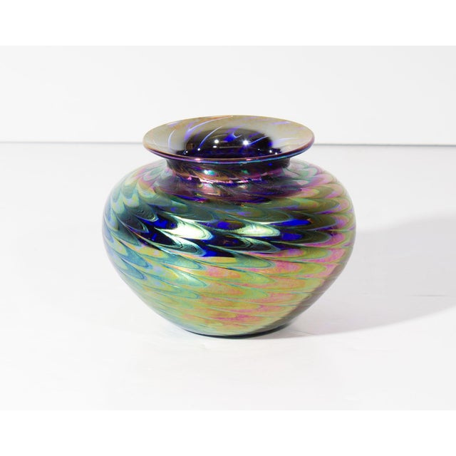 A 1973 art glass vase from Glass Eye Studio. This vase features a low, rounded shape with an iridescent feather pulled...