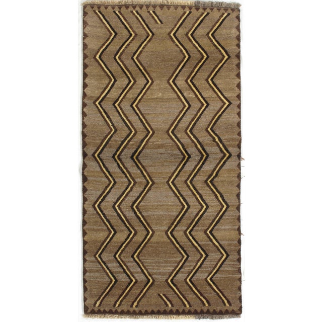 Vintage Persian Gabbeh hand-knotted wool rug featuring a warm camel-brown field decorated with bold repeating zigzag...