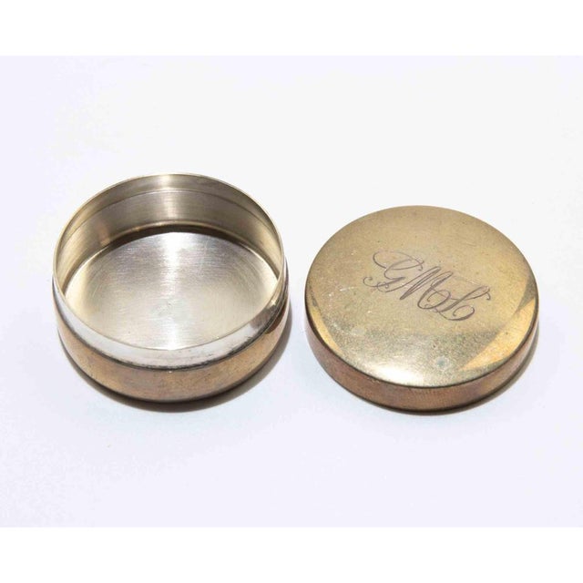 Small circular silvered metal box of clean modernist form with a fitted lid and engraved monogram to the top. The...