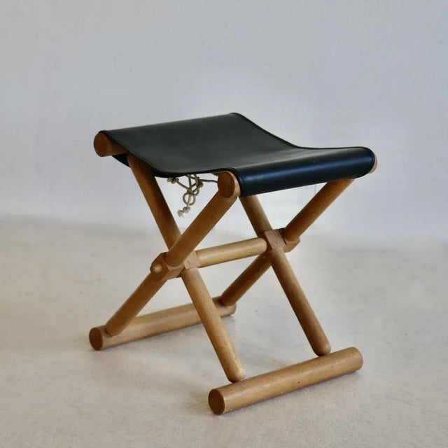 A pair of small folding stools, light wood base, stretched black leatherette seat. France 80s