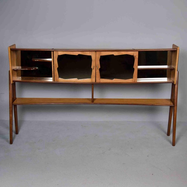 A sculptural bar cabinet in beech, finished in two tones — a deeper stain on the dramatically splayed A-frame legs and...