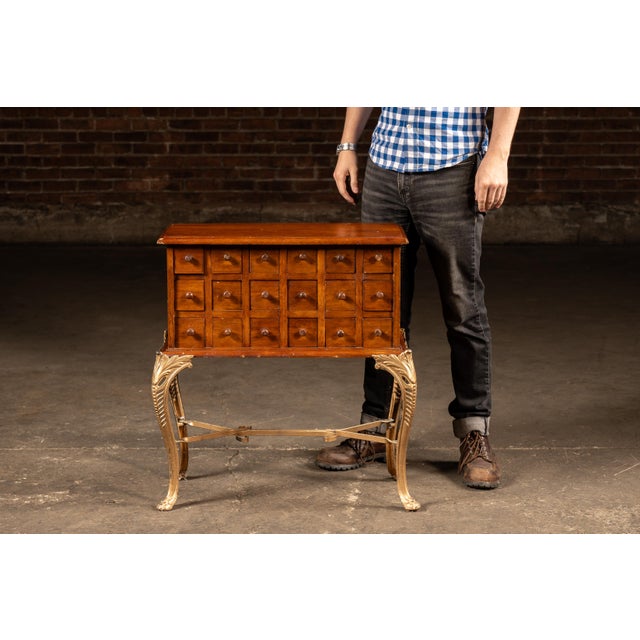 A handsome eighteen-drawer hardwood apothecary-style cabinet elevated on an unusually elaborate cast brass stand. The...