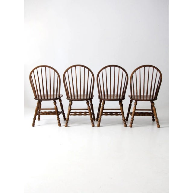 A set of four mid-20th-century Windsor-style dining chairs by Cochrane Furniture. Each chair features a rounded bow back...