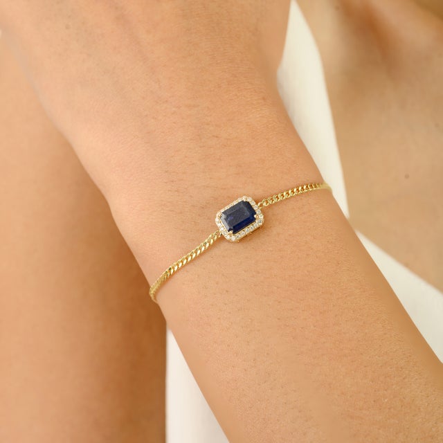 Featuring a stunning 1.58-carat emerald-cut blue sapphire, framed by a sparkling 0.13-carat diamond halo, this bracelet...