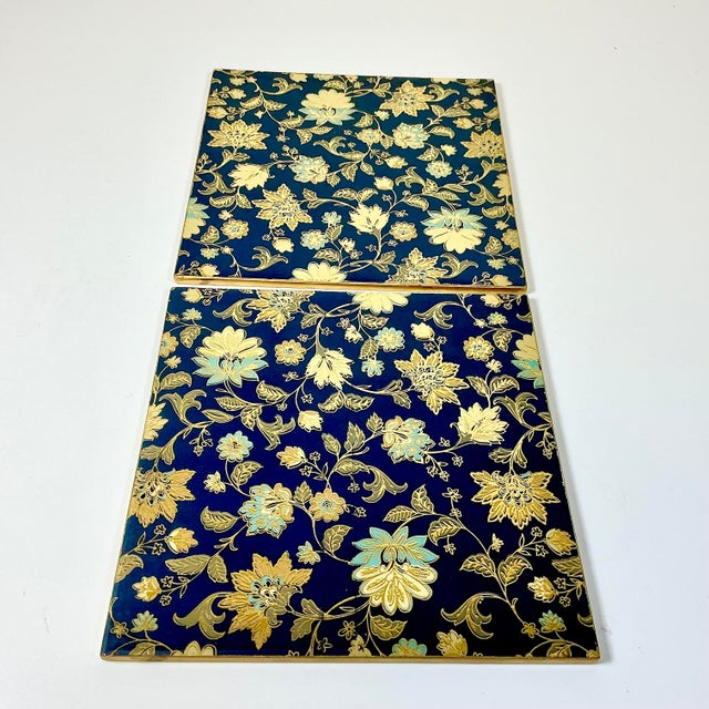 A lovely pair of Chinoiserie flora style wood Trivets. The design has brass-colored gold boarders and accents on an ink...