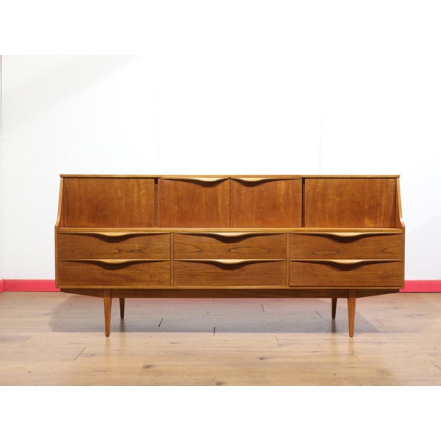 A beautiful credenza by renowned British furniture maker Sutcliffe, this Mid Century Modern Vintage Teak Tall Credenza...