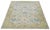 This hand-knotted wool rug features a light blue background with a green border and multicolored all-over designs. This...