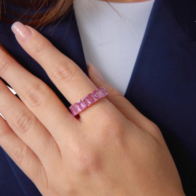 This striking contemporary eternity band showcases a continuous row of 18 emerald cut pink sapphires totaling...
