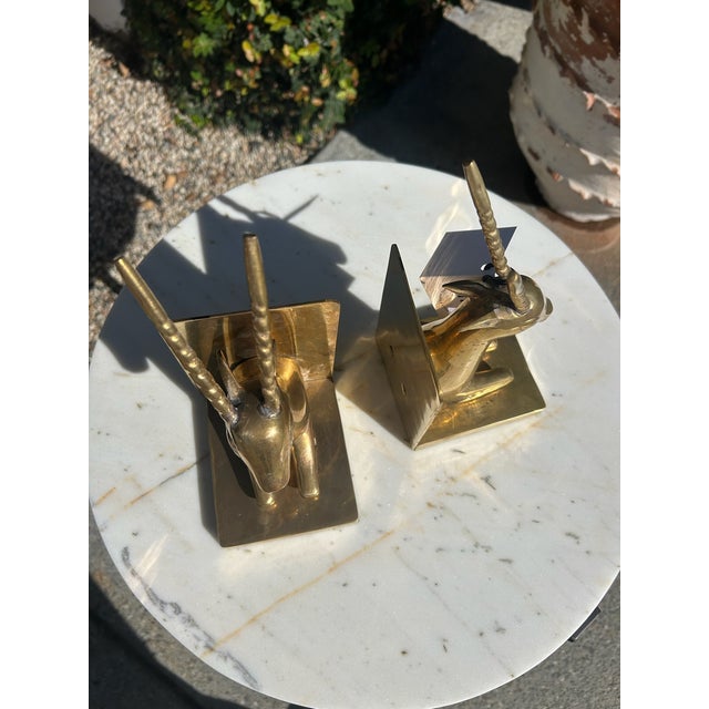 Vintage solid brass antelope bookends featuring sculptural seated antelope forms with elongated horns mounted against...