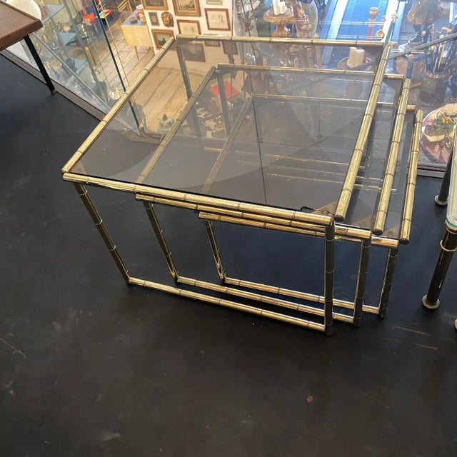 Three brass and smoked glass nesting tables made in Italy in the Sixties in the manner of Tommaso Barbi. Brass it's in...