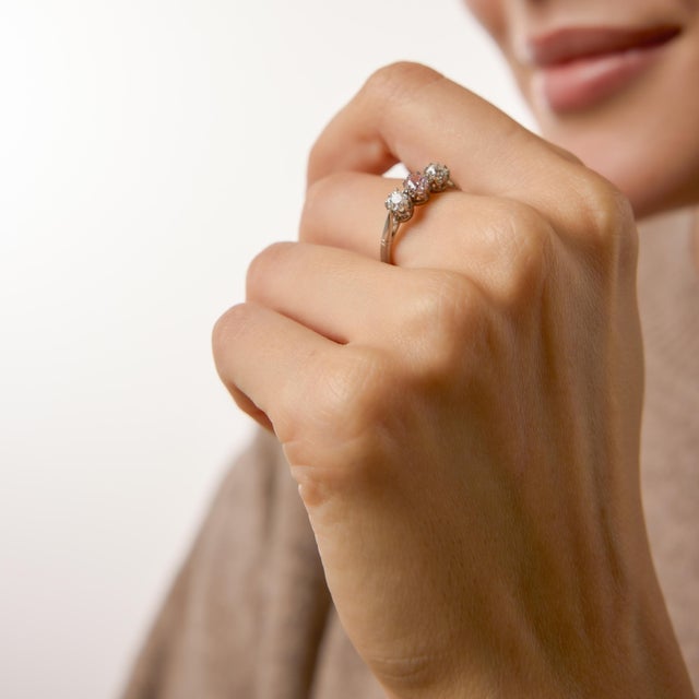 A captivating and romantic design, this vintage three stone ring centers on a rare Fancy pink cushion cut diamond. Its...