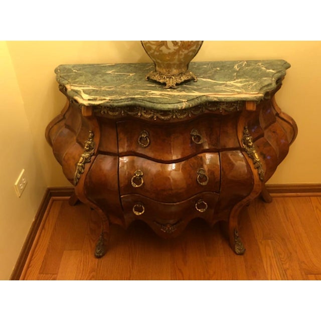 A Louis XV style commode of dramatic bombe form, the swelling front and sides veneered in richly figured burl with cross-...