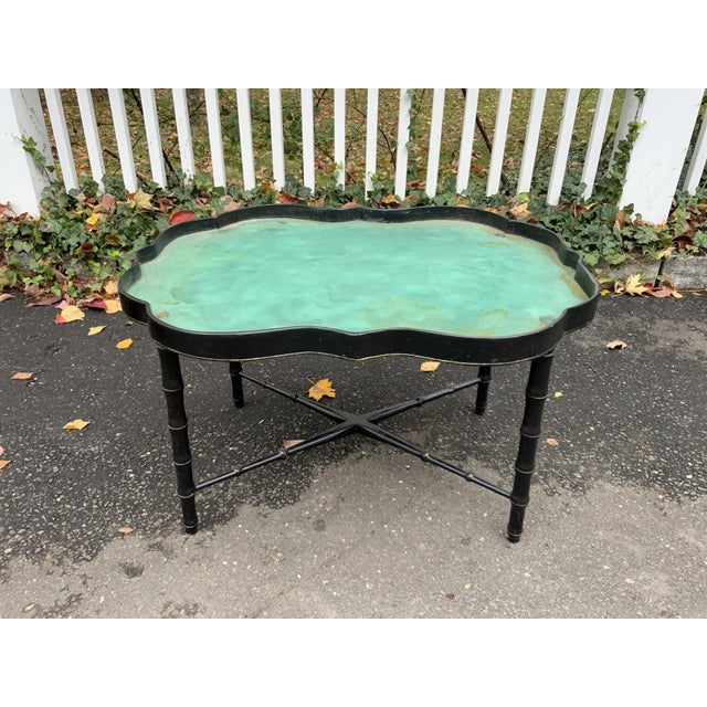 An antique black lacquered tole tray table with a scalloped-shaped edge, gilt trim along the rim and a hand-painted floral...