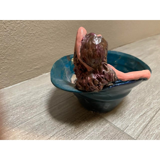 Whimsical pottery bowl with a reclining girl inside a blue bowl. Color is a deep aqua green blue. She is quite pink...