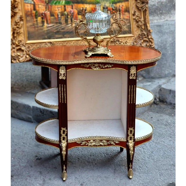 Elegant French Louis XVI-style oval étagère table featuring a richly finished wood structure with ornate gilt bronze and...