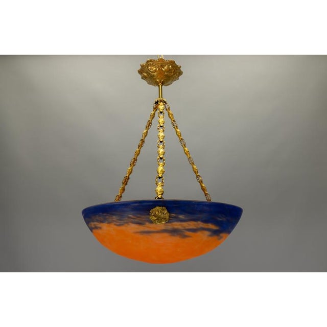 Refined french art nouveau pendant light featuring a richly mottled glass bowl in deep blue and warm amber-orange tones,...