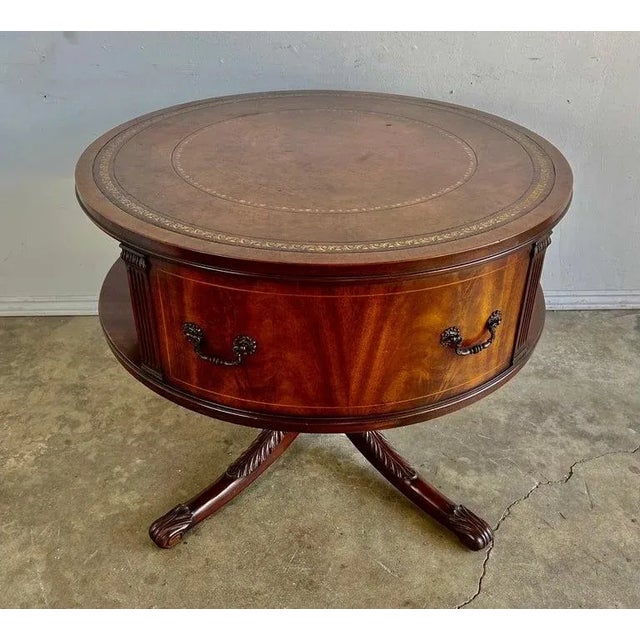 English leather top Drum table that stands on a four curved legs with carved acanthus leaf detail. The brown leather on...