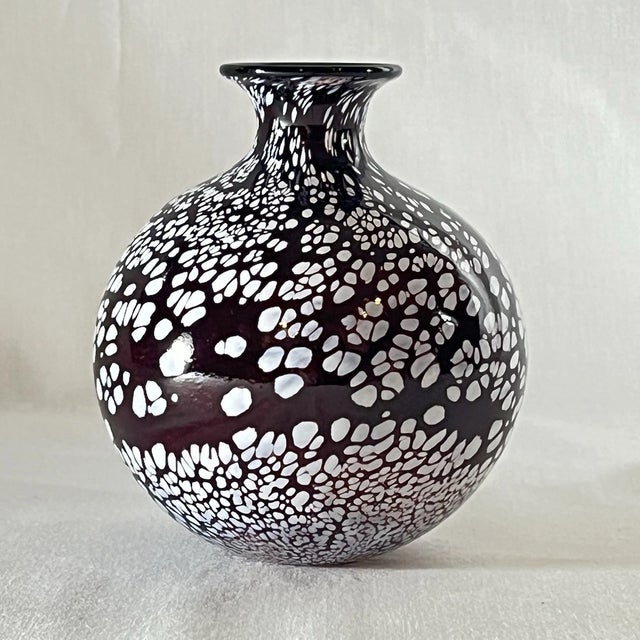 A beautiful hand-blown art glass vase featuring a rich dark purple base accented with white confetti-style speckling...