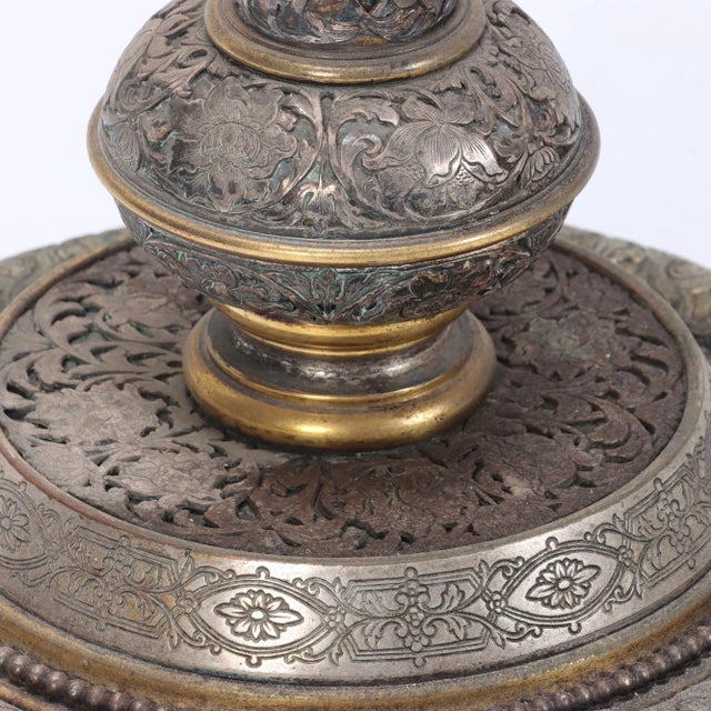 The columnar standard is composed of a series of turned and banded sections, richly chased and engraved with scrolling...