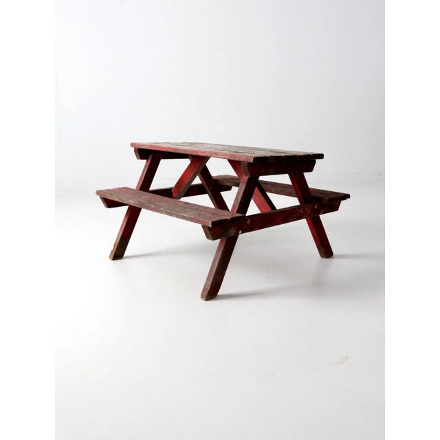 This is a vintage children's picnic table. The rustic red wooden table features connected bench seats and a slat wood top....