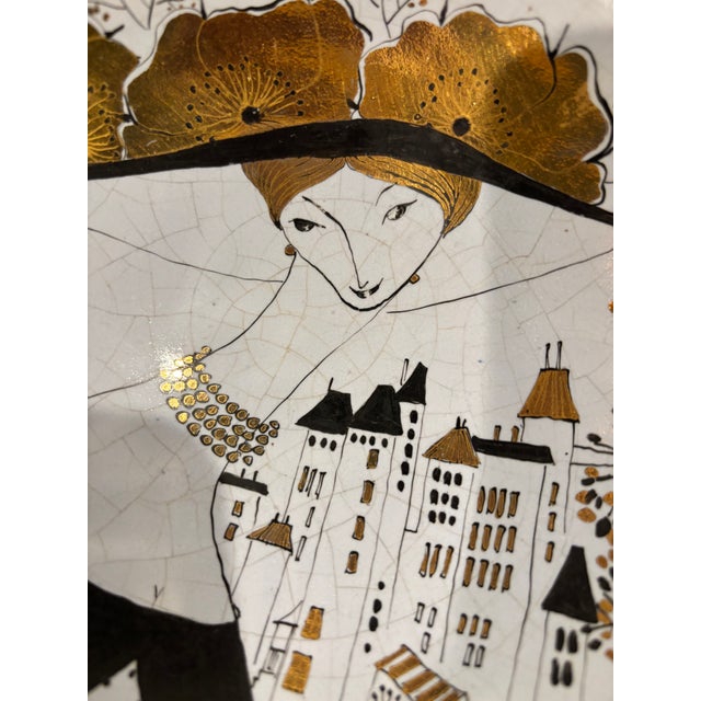 A sophisticated mid-century French hand-painted ceramic dish featuring a graphic, urban-inspired illustration accented...