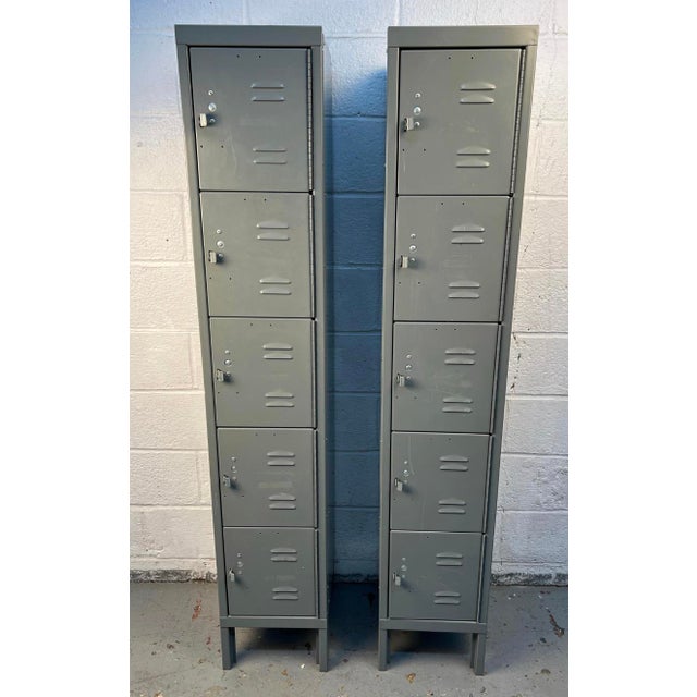 A pair of tall industrial metal foot lockers, each featuring five spacious compartments for ample storage. Their rugged...