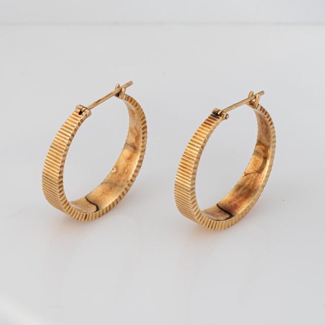 Fine detailed pair of oval 'shimmer' hoop earrings crafted in 14k yellow gold (circa 1980s to 1990s). The stylish earrings...