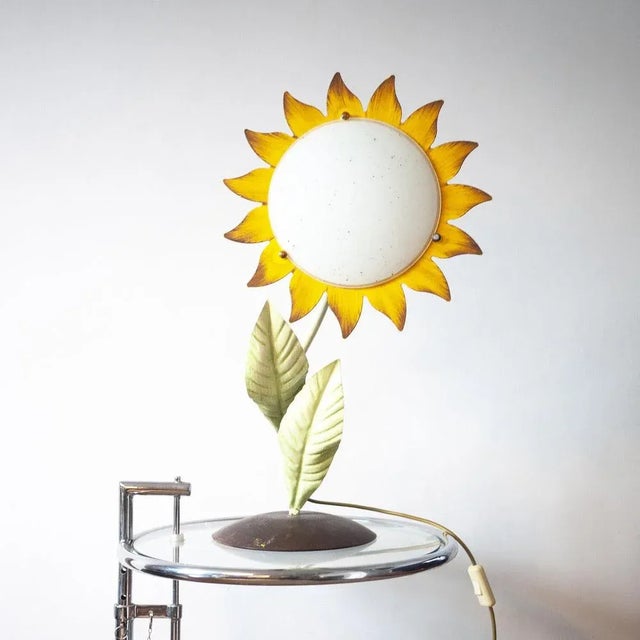 A 1970s hand painted metal sunflower desk lamp. The lamp sits on a round base and has an on/off switch attached to the...