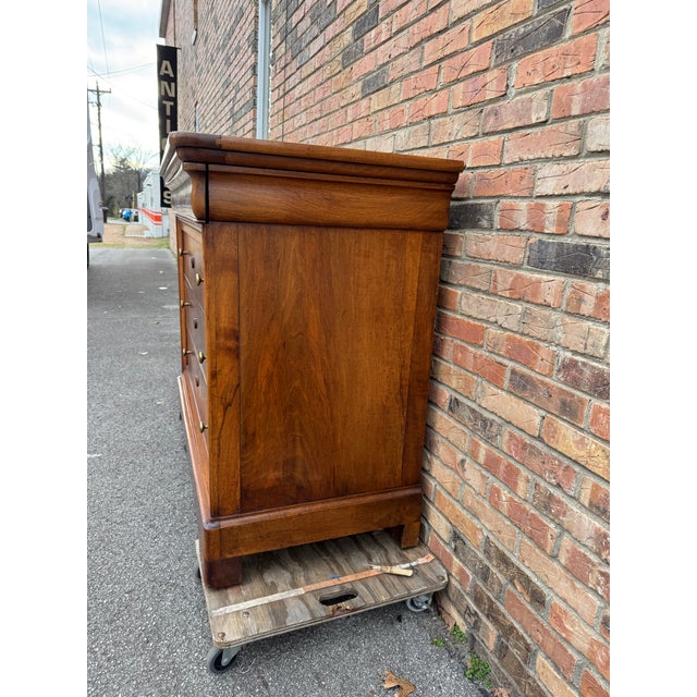 An elegant antique chest of drawers showcasing beautifully figured walnut veneer, warm patina, and classic brass pulls....