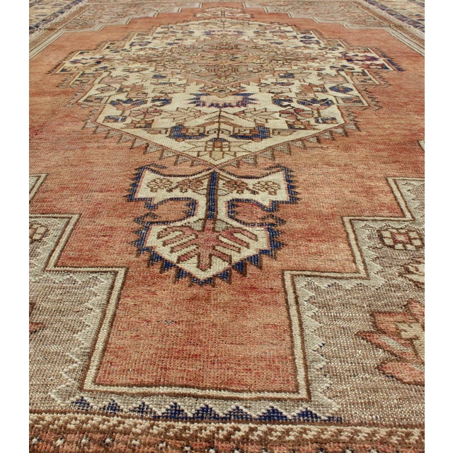 This beautiful Turkish Oushak Rug has a medium blue color with a light orange background. The center medallion has earth...
