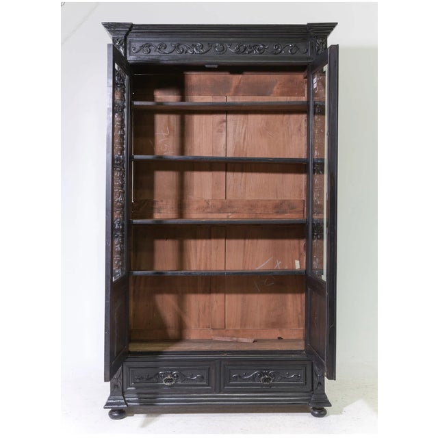 This 19th C French bookcase cabinet features intricate scrollwork and hand-carved details finished in an ebonized...