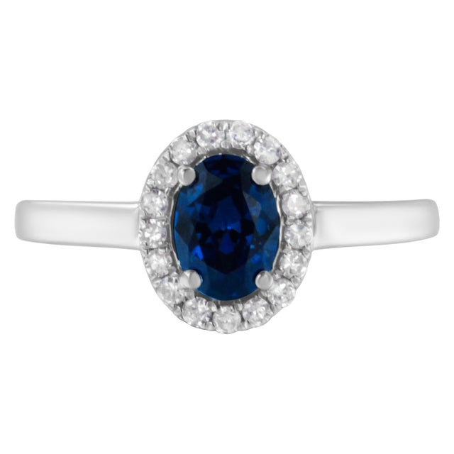This dazzling 10k white gold ring features a 1 1/4ct deep blue oval sapphire. A brilliant halo of 1/5ct round cut diamonds...