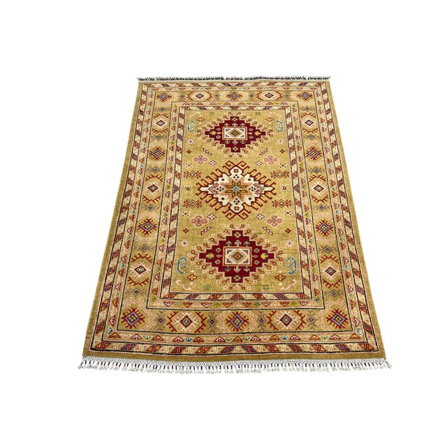 This Kazak style wool rug has three bold medallions across a golden beige field. Burgundy, cream, soft pink, and blue...