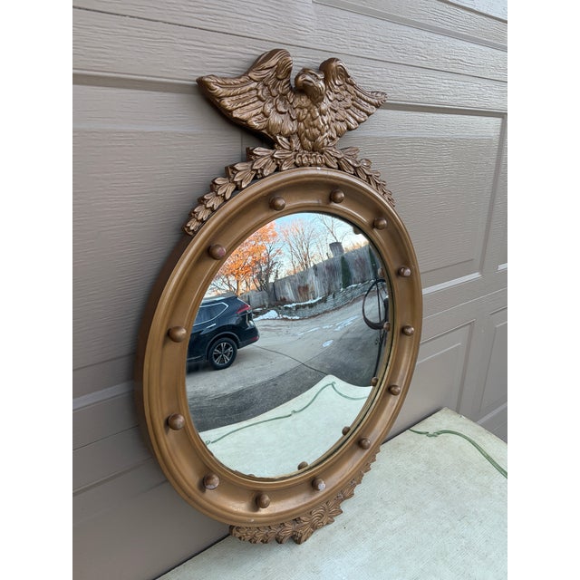 A gorgeous Federal or Regency style convex bullseye wall mirror featuring a carved eagle with open wings standing on olive...