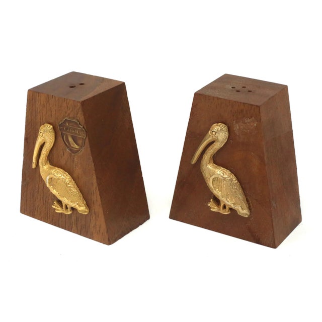 A set of vintage salt and pepper shakers, made of wood with gold-colored metal embossed pelicans. One shaker says "Myrtle...