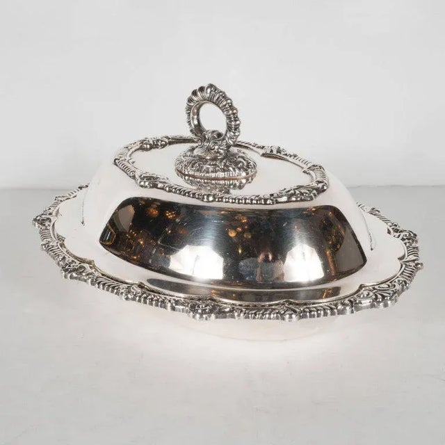 This stately sterling silver plated tureen features a reeded handle, scalloped edges with Baroque details, including fleur...