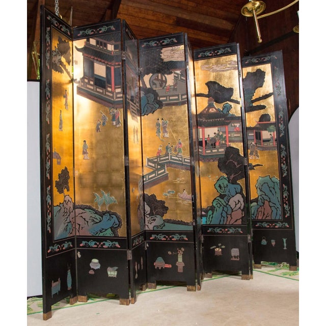 A grand eight panel Coromandel screen. The screen has mostly a gilt background with a few architectural structures and...
