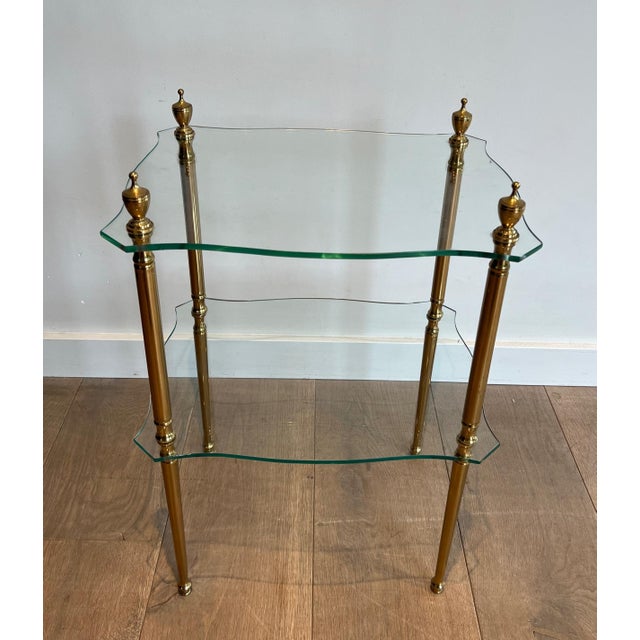 This attractive neoclassical-style side table is made of brass and features two glass shelves. It is a French work by...