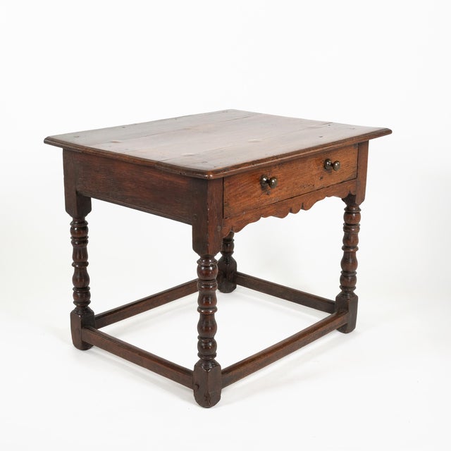 17th-century English oak side table with a single drawer and shaped apron. The drawer front with a pair of wooden knobs...