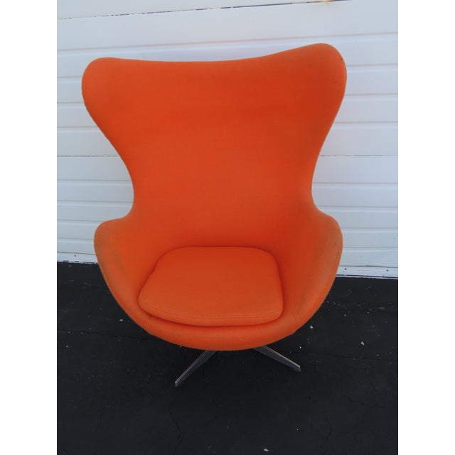 This vintage Egg-style lounge chair features a striking orange upholstered shell with a sturdy metal swivel base. Inspired...