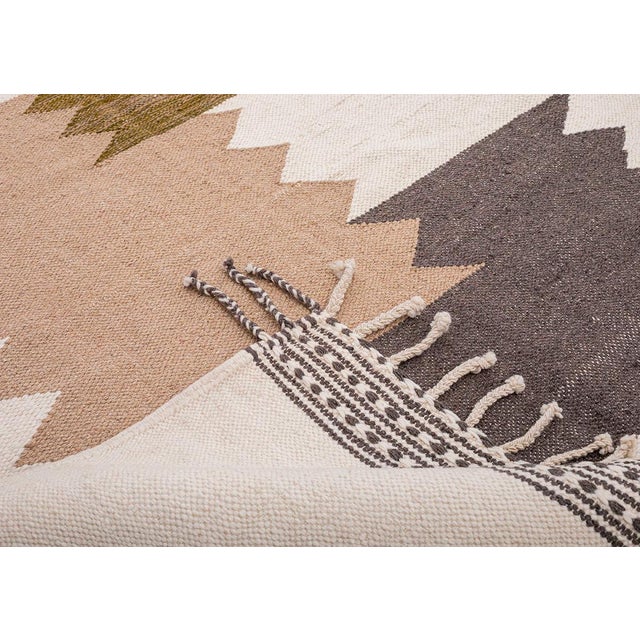 Bold zigzag-edged bands interlock down the center of this handwoven rug, mustard yellow, sand beige, and charcoal grey...