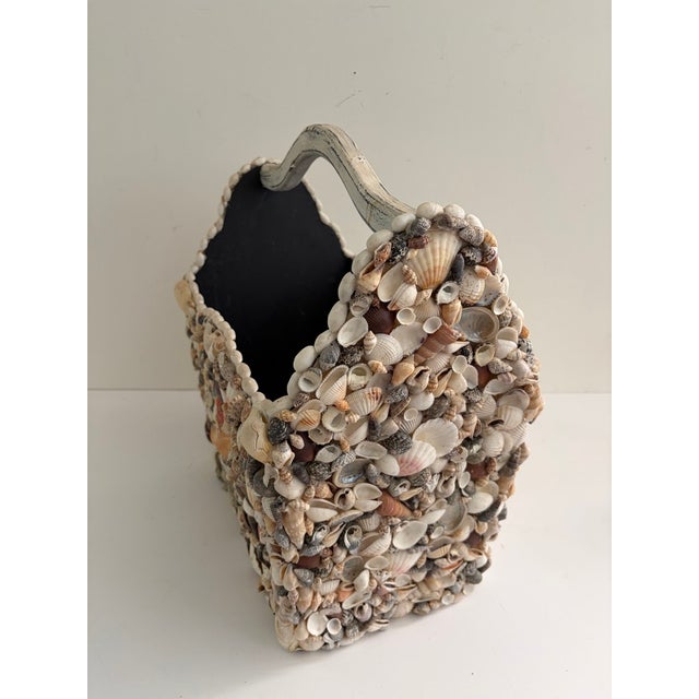 Large vintage wooden basket covered with natural seashells, including scallop shells, spiral shells, and assorted beach...